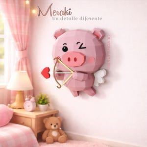 Puede incluir: Decoración de pared con forma de cerdo geométrico rosa, con arco y flecha, un corazón rojo y pequeñas alas blancas. El cerdo guiña un ojo y tiene una gran nariz rosa. El texto "Meraki" y "Un detalle diferente" están en la parte superior.