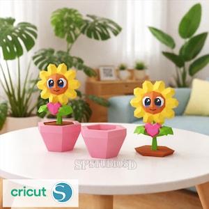 Puede incluir: Dos girasoles de papel con pétalos amarillos, centros naranjas y caras sonrientes. Uno está en una maceta rosa, el otro sobre una base marrón. También hay una tercera maceta rosa. El texto "SPSTUDIO3D" y "cricut" son visibles.
