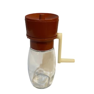 Op de afbeelding: Een heldere glazen kruidenmolen met een bruine plastic bovenkant en een crèmekleurige hendel. De molen heeft een klassiek ontwerp, geschikt voor het malen van diverse kruiden. De glazen pot is leeg.