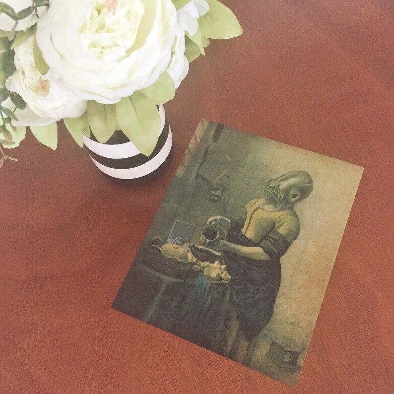 May include: A vintage-style print of a woman pouring a pitcher of liquid into a bowl. The woman has a fish head and is wearing a yellow and blue dress. The print is on a light brown background.