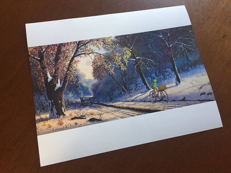 May include: A print of a winter landscape featuring a snow-covered road and trees. A figure on a red bicycle with a basket rides along the road. The artwork has a serene, naturalistic style with muted colors.