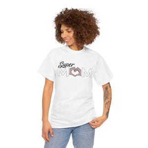 May include: A white short-sleeved t-shirt featuring the black text Super and the word MOM in outline font. The letter O in MOM is replaced by a heart shape formed by two hands with a colorful, intricate floral pattern inside the heart design.