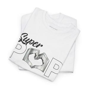 May include: White t-shirts with the words "Super Pop" in black script and outline letters. The letter "O" is replaced with a heart shape formed by two hands in a silver metallic color. The text "look don't get shook" is printed on the collar.