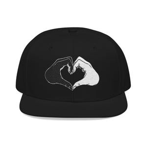 May include: A black snapback cap featuring an embroidered graphic on the front panel. The design displays two hands forming a heart shape, with one hand rendered in black thread and the other in white thread, creating a high-contrast visual effect.