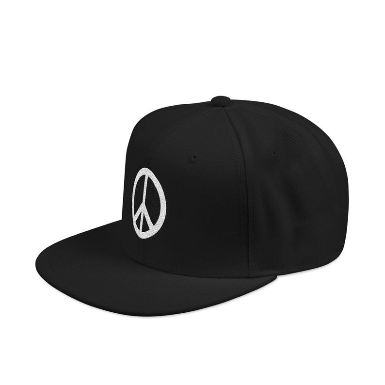 May include: A black baseball cap featuring a white embroidered peace sign symbol centered on the front panel. The cap has a structured crown, a flat brim, and a button at the top center. The design is clean, simple, and monochromatic in style.