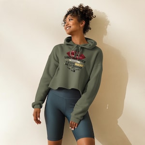 May include: An olive green cropped hoodie featuring a graphic of red lips and the Spanish text "DIME CON QUIEN ANDAS Y SI ESTA BUENO ME LO MANDAS" with a small smartphone icon and the word "SEND" printed in black on the center of the chest.