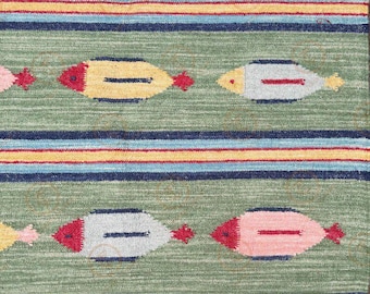 Könnte beinhalten: Nahaufnahme eines grünen Teppichs mit Streifenmuster. Der Teppich hat horizontale Streifen in Blau, Gelb und Rot. Fischförmige Designs in Gelb, Grau und Rosa sind gleichmäßig über den Teppich verteilt.