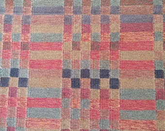 Könnte beinhalten: Nahaufnahme eines gewebten Stoffes mit einem Karomuster. Das Design zeigt ein Gitter aus abwechselnden Quadraten und Rechtecken in Rot-, Blau-, Grün- und Beigetönen. Die Textur des Stoffes ist sichtbar, was auf ein strukturiertes Gewebe hindeutet.