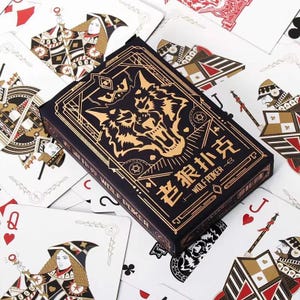 Puede incluir: Una baraja de cartas con una caja negra con un diseño de lobo dorado y el texto "WOLF POKER". Las cartas están esparcidas alrededor de la caja, mostrando varios palos y figuras.