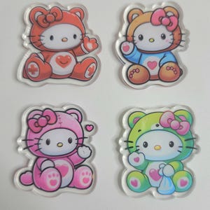 May include: Four clear acrylic charms featuring a cartoon cat character in different animal costumes. The costumes are a red bear, a brown bear, a pink bear, and a green bear. Each charm has a bow and heart details.
