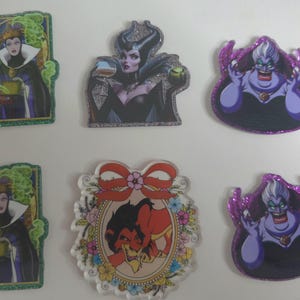 May include: A collection of six acrylic pins featuring Disney villains. The pins include images of the Evil Queen, Maleficent, Ursula, and Scar. The pins have glitter accents and are in various shapes and sizes.