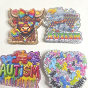 May include: Four glittery pins with autism awareness themes. One features a Highland cow with sunglasses and a lollipop. Another shows Dumbo the elephant with the word "AUTISM." The third is a puzzle piece design with the word "AUTISM." The last is a heart with ribbons.