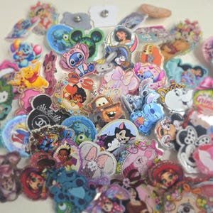 May include: A collection of colorful character pins featuring Disney and other cartoon characters. The pins include images of Mickey Mouse, Stitch, Winnie the Pooh, and other popular characters. The pins are various shapes and sizes, with a glossy finish.