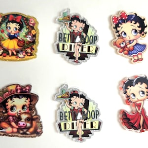 May include: A collection of six colorful cartoon character stickers. The stickers feature Snow White, Betty Boop in various poses, and Betty Boop Diner. The stickers have glittery accents and are on a white background.