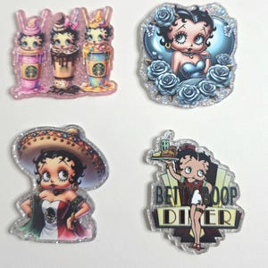 May include: A collection of four glittery acrylic charms featuring Betty Boop and themed designs. One charm shows three Betty Boop characters with Starbucks-style drinks. Other charms depict Betty Boop in various outfits, including a diner uniform and a Mexican-inspired dress.