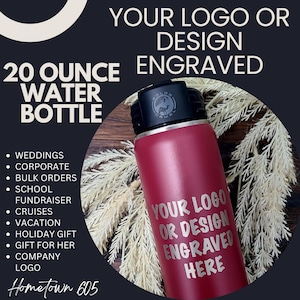 May include: A 20 ounce red water bottle with a black lid and a silver engraved design that says "Your Logo or Design Engraved Here". The bottle is sitting on a wooden surface with a white, feathery plant in the background.