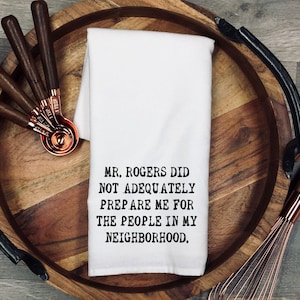 May include: White kitchen towel with black text that reads "MR. ROGERS DID NOT ADEQUATELY PREPARE ME FOR THE PEOPLE IN MY NEIGHBORHOOD."