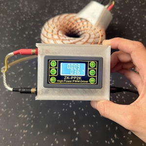 Può includere: Una custodia di plastica trasparente contiene un display digitale con la scritta "ZK-PP2K High Power PWM Driver". Il display mostra letture numeriche. Sono visibili anche una bobina di rame e fili con connettori rossi e gialli.