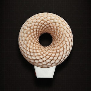 Pode incluir: Uma luz noturna decorativa com um design em forma de toroide tecido creme com detalhes dourados. A luz noturna está sobre uma base branca contra um fundo escuro.