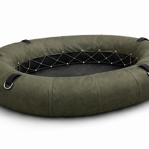 Puede incluir: Una balsa inflable verde oliva con un diseño circular. La balsa tiene correas negras y anillos metálicos para asegurar objetos. El interior presenta una base negra y una red de cuerda blanca. Diseñada para actividades acuáticas.