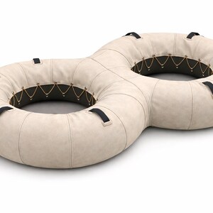 Puede incluir: Un flotador de piscina inflable beige en forma de ocho con asas negras. El interior del flotador es negro con detalles decorativos dorados. El flotador está diseñado para la relajación y el ocio en el agua.