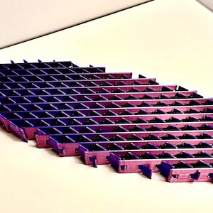 May include: A geometric, multi-tiered structure with a gradient of purple and pink hues. The object is composed of numerous small, rectangular compartments, creating a grid-like pattern. The design suggests a decorative or functional item, possibly for display or storage.