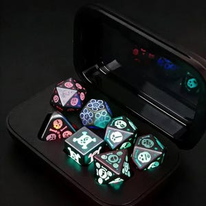 Peut inclure: Un ensemble de sept dés polyédriques noirs avec des motifs verts et bleus brillants, dont des crânes et des motifs géométriques, à l'intérieur d'un étui noir. Les dés sont conçus pour les jeux de rôle sur table.
