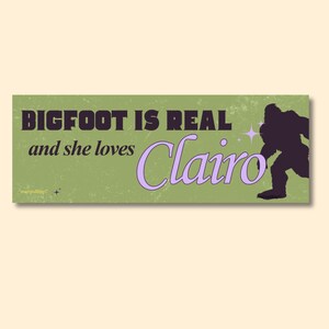 Może przedstawiać: Zielona prostokątna naklejka z napisem "BIGFOOT IS REAL and she loves Clairo". Tekst jest w mieszance fioletowych i ciemnofioletowych czcionek. Sylwetka Bigfoota znajduje się po prawej stronie naklejki.