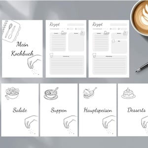 May include: A collection of white recipe pages with black line art illustrations. The pages include the text "Mein Kochbuch" and recipe templates. Individual cards feature food categories like "Salate" and "Desserts". A cup of coffee and a pen are also visible.