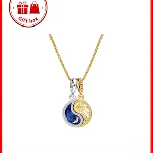 Puede incluir: Un collar de cadena dorada con un colgante con un diseño de yin-yang. Una mitad del colgante es un cielo nocturno azul oscuro con una luna creciente y estrellas, y la otra mitad es un sol con un diamante en el centro. El colgante está delineado con detalles plateados y dorados.