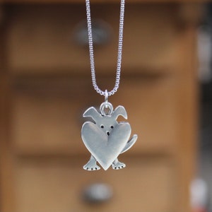 May include: A silver necklace with a charm of a dog holding a heart in its paws.