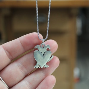 May include: A silver necklace with a pendant shaped like a dog holding a heart in its paws.