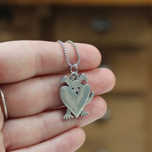 May include: Silver necklace with a charm of a dog holding a heart in its paws.
