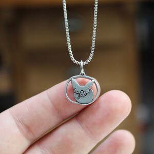 May include: A silver chain necklace with a pendant featuring a stylized image of a fox curled up inside a circle.