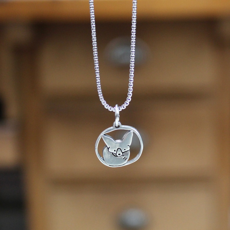 May include: A silver necklace with a round pendant featuring a stylized image of a fox's head.
