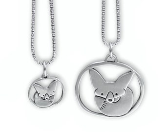 May include: Two silver necklaces with fox pendants. The larger pendant is oval shaped and features a fox curled up inside. The smaller pendant is round and features a fox's head.