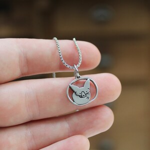 May include: A silver necklace with a circular pendant featuring a stylized image of a pig's face.