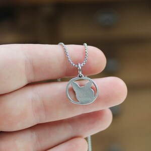 May include: A silver chain necklace with a circular pendant featuring a cut-out silhouette of a cat's head.