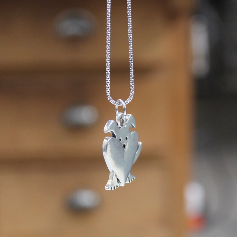 May include: A silver necklace with a pendant shaped like two figures holding a heart. The pendant is detailed and has a smooth, polished finish.