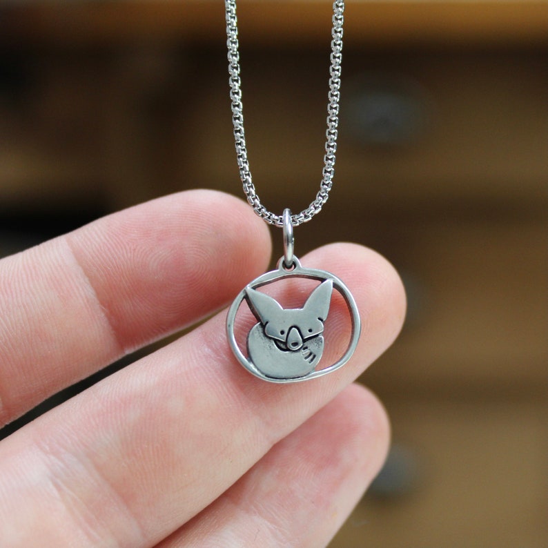 May include: A silver necklace with a pendant featuring a stylized fox curled up in a circle.