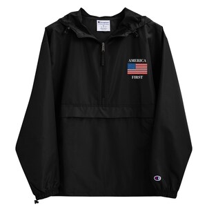 Könnte beinhalten: Schwarze Champion Anorak-Jacke mit Kapuze und halbem Reißverschluss. Auf der Brust ist der Schriftzug "AMERICA FIRST" mit einer amerikanischen Flagge abgebildet. Kleines Champion-Logo auf dem linken Ärmel.