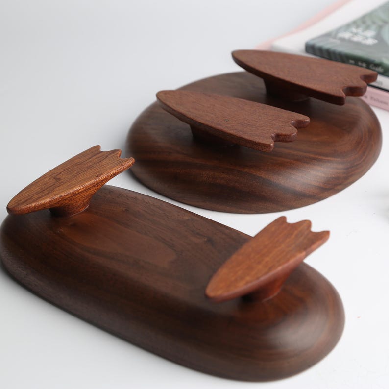 May include: Two wooden serving trays with a dark brown finish. Each tray has a rounded shape with a raised, leaf-shaped handle. The trays are made of a rich, dark wood and are displayed on a white surface.