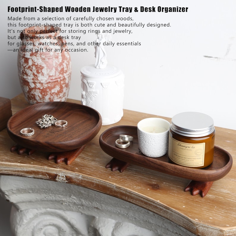 May include: Footprint-shaped wooden jewelry tray and desk organizer. The dark brown trays are made of wood and have a footprint design. One tray holds rings, and the other holds a candle and a jar.
