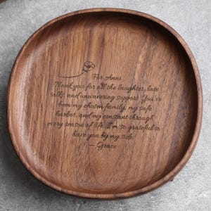 May include: A round, wooden serving tray with a dark brown finish. The tray has a carved floral design and engraved text that reads "For Anni" followed by a heartfelt message and the name "Grace".