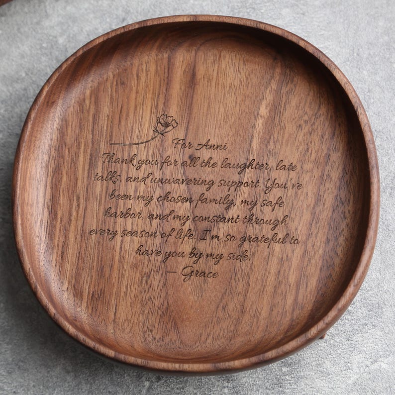 May include: A round, wooden serving tray with a dark brown finish. The tray has a carved floral design and engraved text that reads "For Anni" followed by a heartfelt message and the name "Grace".