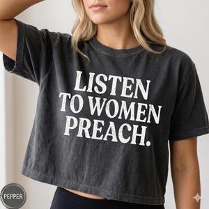 May include: Dark gray cropped t-shirt with the text "LISTEN TO WOMEN PREACH." in white block letters. The shirt has a vintage, slightly faded appearance.