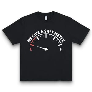 Könnte beinhalten: Schwarzes T-Shirt mit weißer Grafik einer Anzeige, die "MY GIVE A SH*T METER" anzeigt. Die Nadel der Anzeige zeigt auf das "E" für leer. Das T-Shirt hat einen Rundhalsausschnitt.