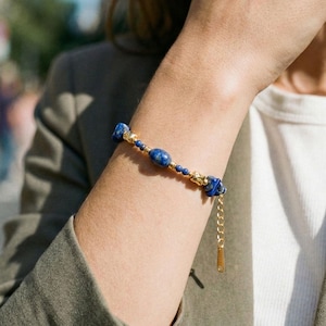 Könnte beinhalten: Ein blaues Perlenarmband mit goldenen Akzenten. Das Armband besteht aus einer Mischung aus runden und unregelmäßigen blauen Perlen, die durch goldfarbene Kettenglieder verbunden sind. Eine goldfarbene Verlängerungskette ist angebracht. Das Armband wird am Arm getragen.