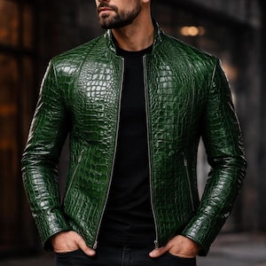 May include: A green leather jacket with a textured, crocodile-like pattern. The jacket has a zip-up front and a stand-up collar. The person in the image is wearing a black shirt and black jeans.