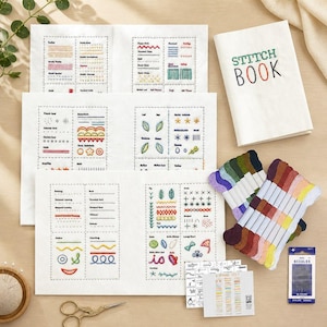 Puede incluir: Un conjunto de suministros de bordado, que incluye diagramas de puntadas, un "STITCH BOOK", madejas de hilo y agujas. Los diagramas muestran varios tipos de puntadas con ejemplos de hilo de colores. También hay unas tijeras doradas y un bastidor de bordado de madera.